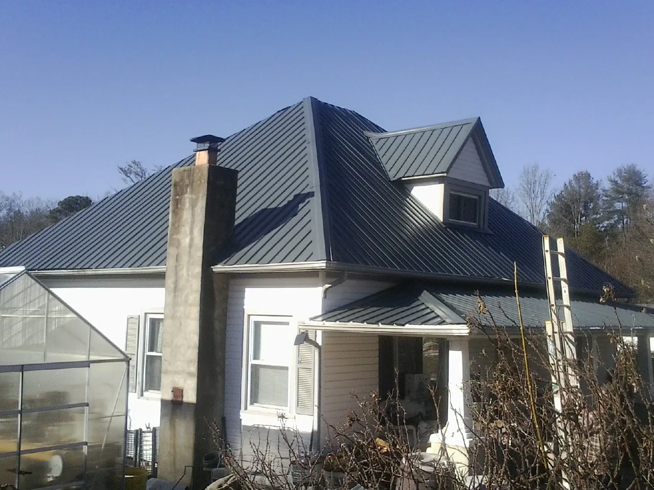 Dark blue standing seam metal roof on a white farmhouse with dormer — Slate & Tile Roof Repair by Roofing Brothers in Lineville