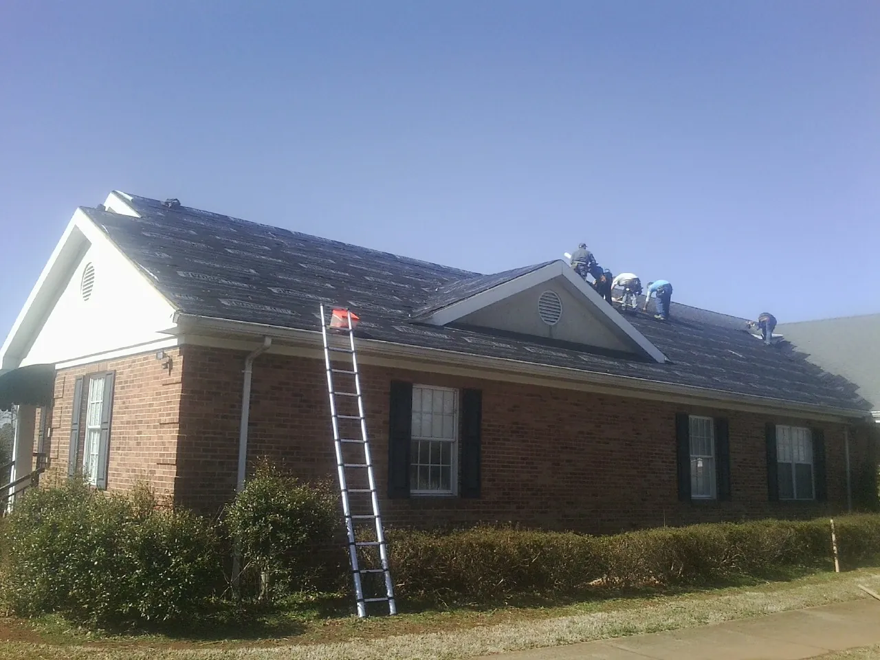 Crew tearing shingles off a brick ranch roof with a ladder set — Metal Roof Repair work by our crew in Lineville
