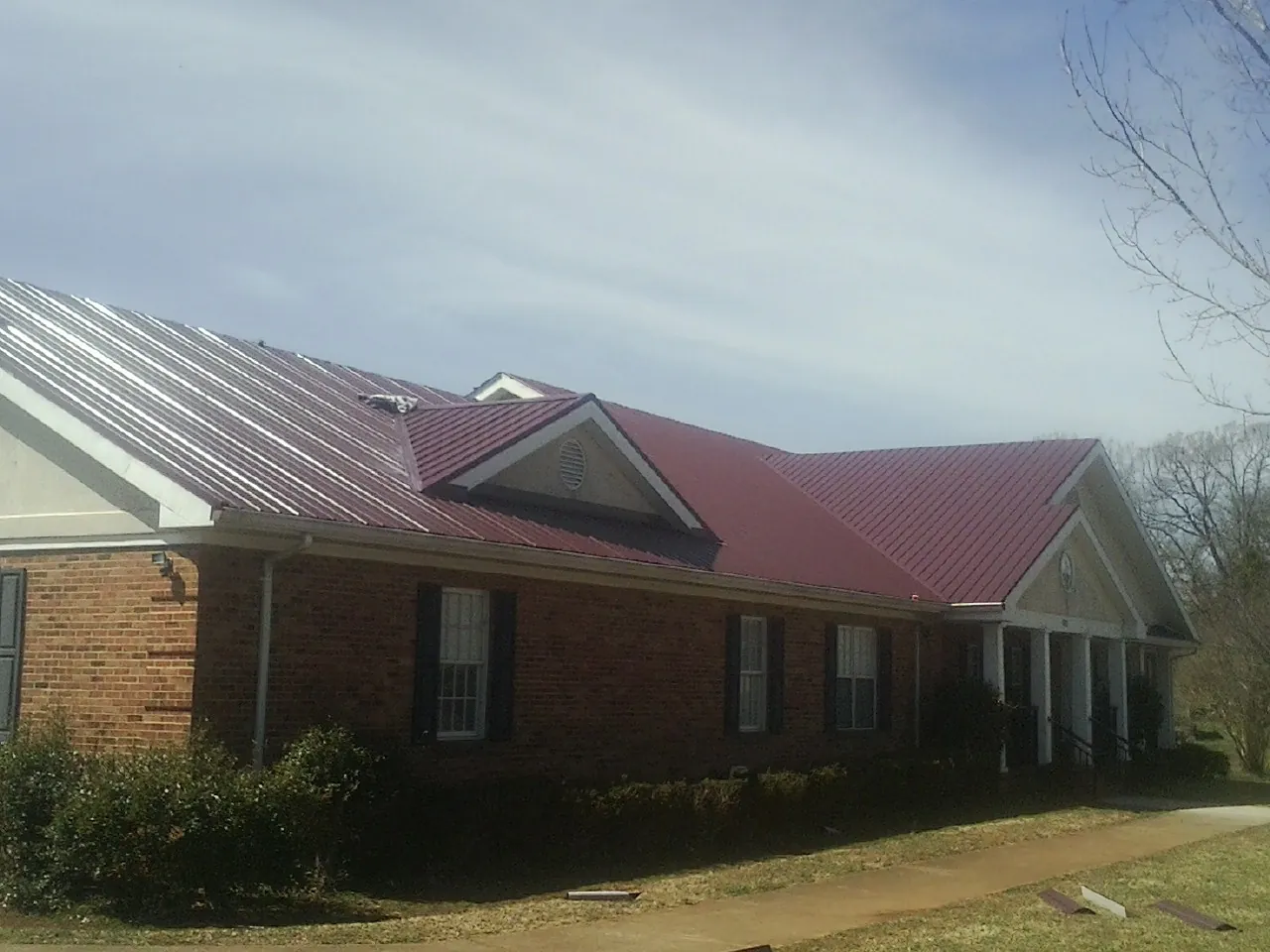 Red metal roof with gabled entries on a long brick building, from a Hail Damage Roof Repair job in Lineville