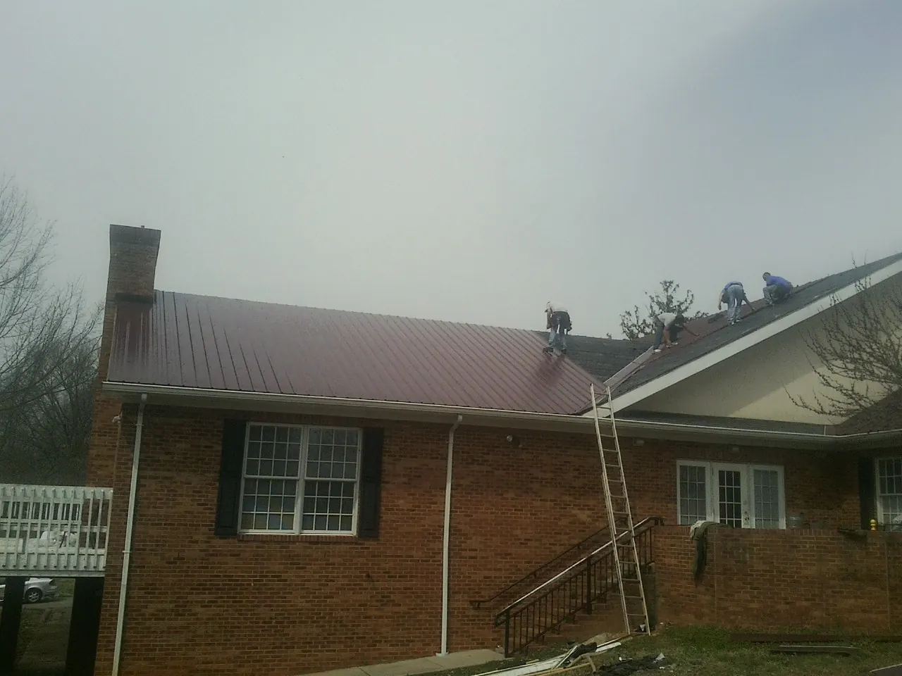 Crew setting red metal roofing panels on a brick home in Lineville