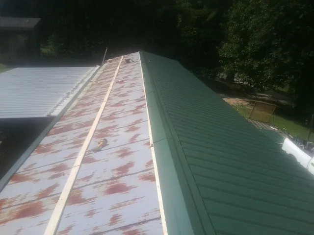 Old rusted panels beside newly installed green metal roofing — Wind Damage Roof Repair by Roofing Brothers in Lineville