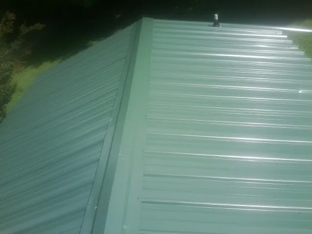 New green metal panels meeting at the ridge of a roof — Flat Roof Repair work by our crew in Lineville