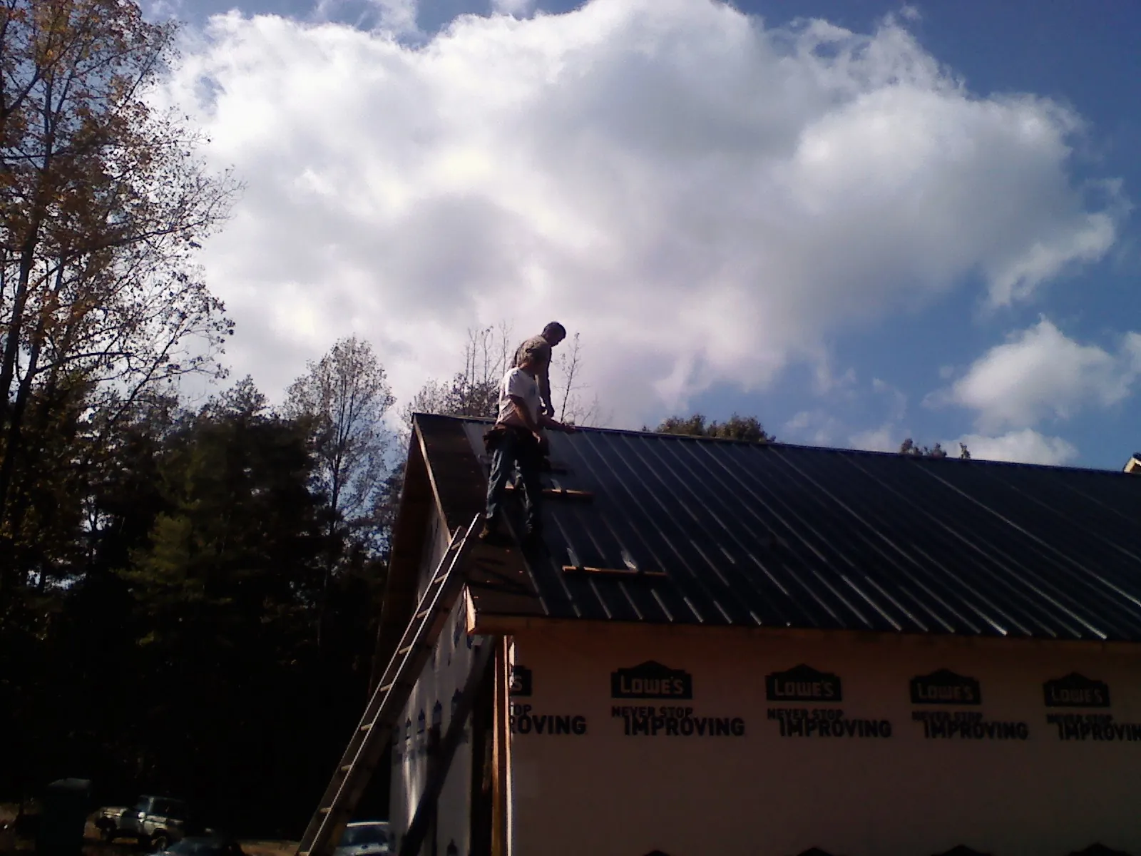 Roofer fastening dark metal panels high against a cloudy sky, from a Roof Inspection job in Lineville