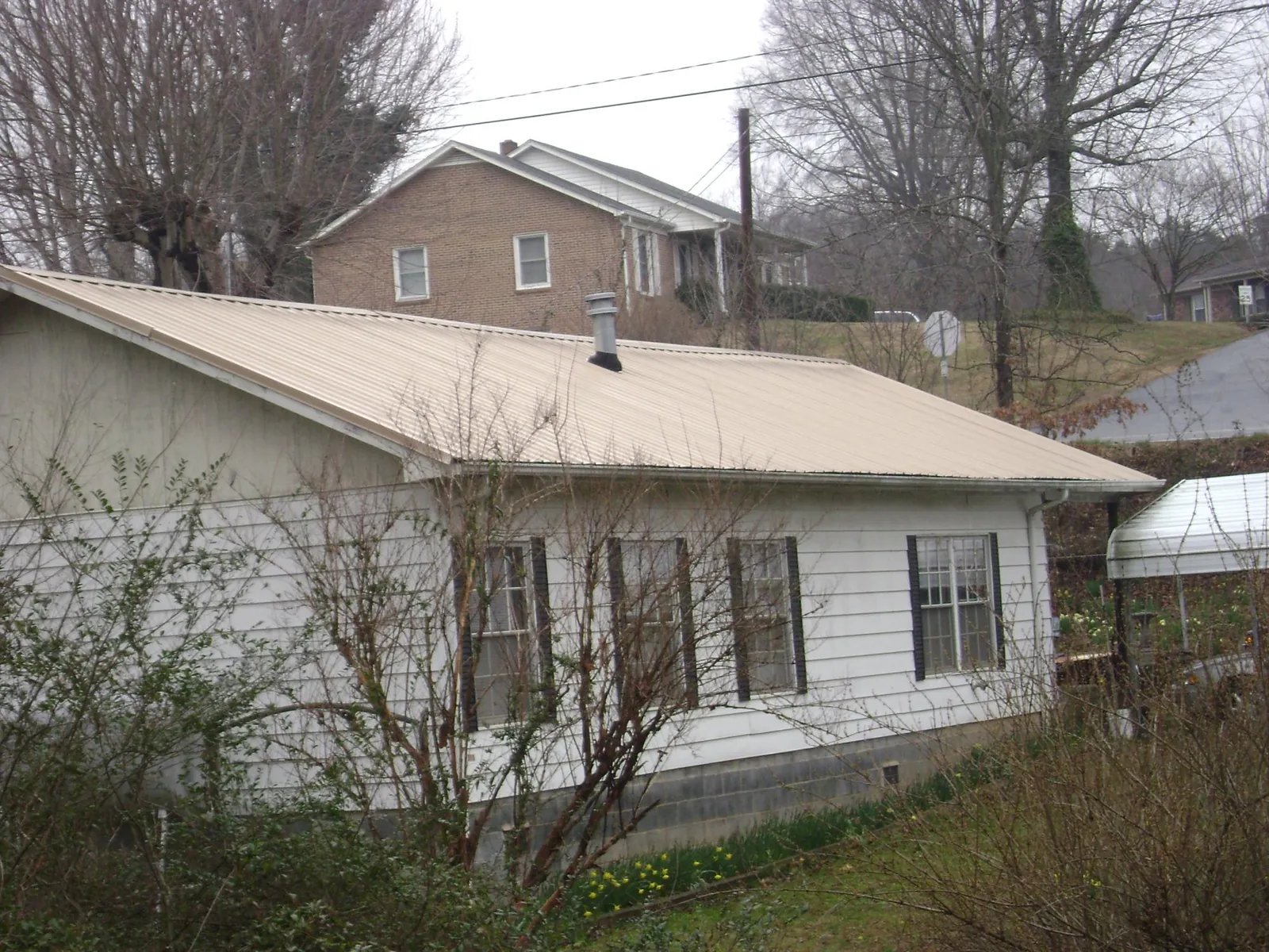 Tan metal roof on a white sided house set into a hillside — Commercial Roofing by Roofing Brothers in Lineville
