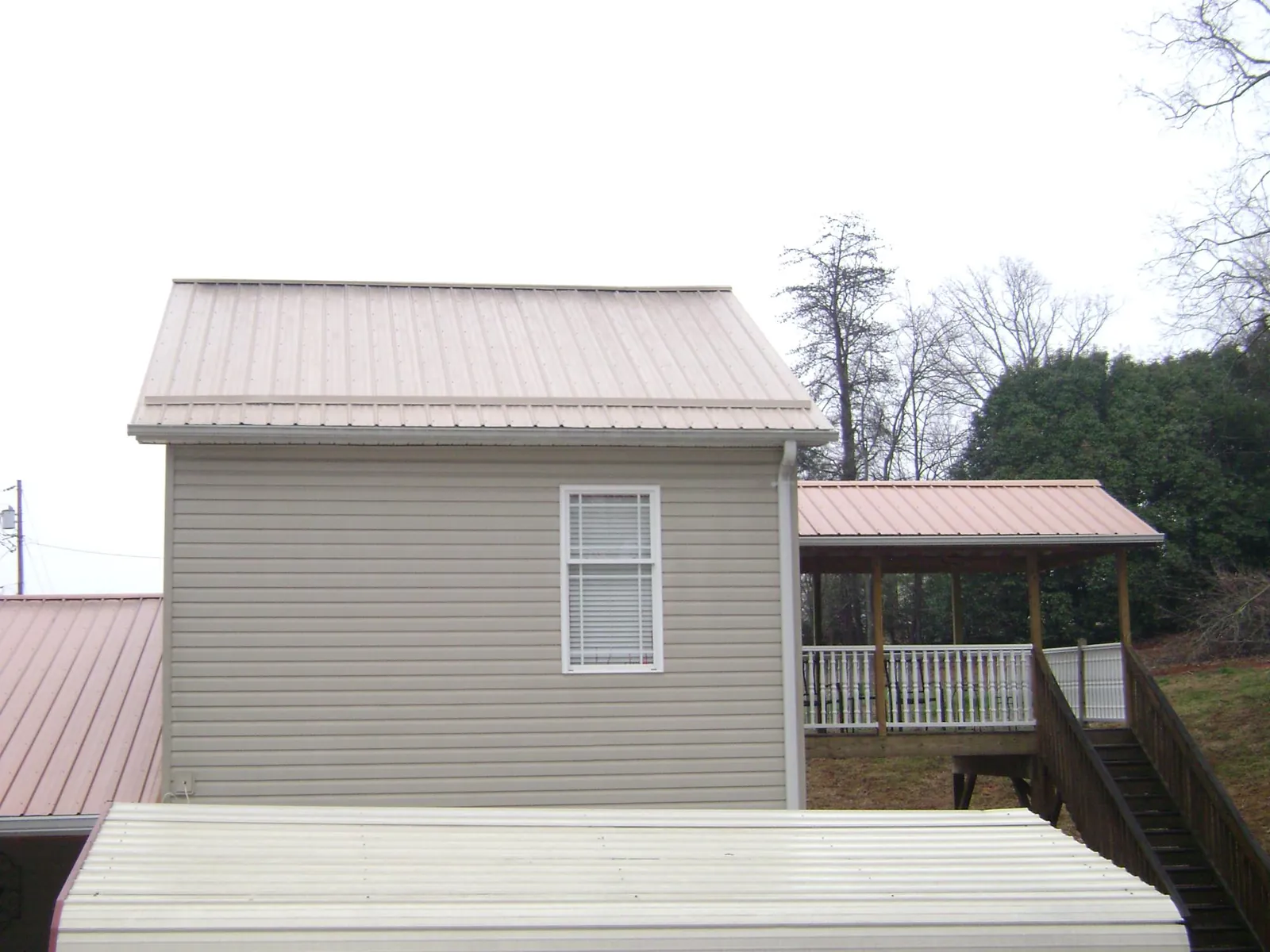 Tan metal roofs on a two story addition and attached porch, from a Roof Replacement job in Lineville